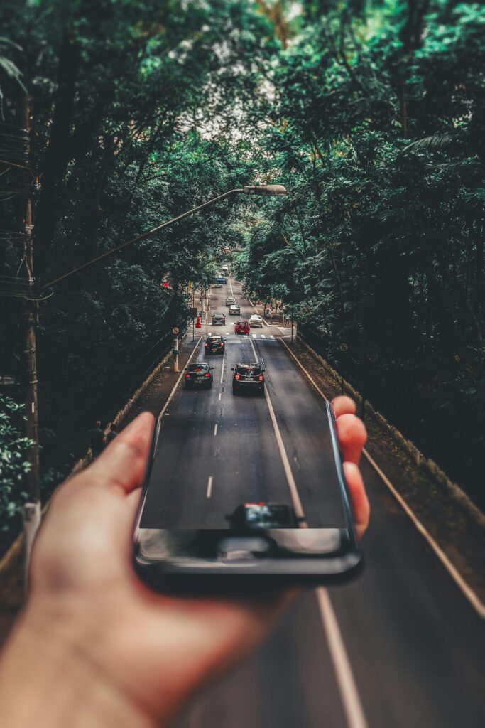 Forced Perspective Photography of Cars Running on Road Below Smartphone